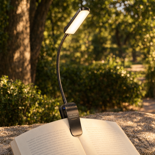The Book Collective branded gooseneck clip reading light, matching the user's selected Alibaba design, illuminating an open book in a warm park setting.